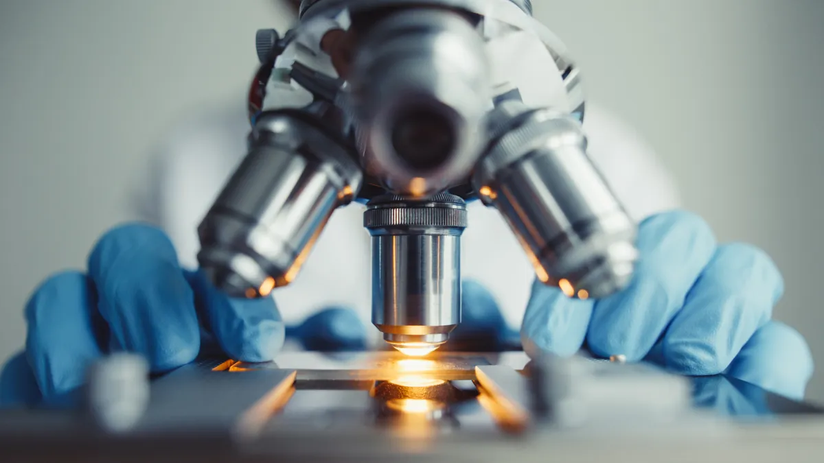 Close-up of a person with blue latex gloves arranging a glass plate in a microscope