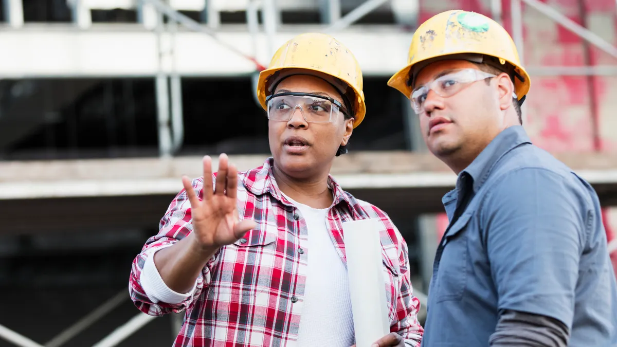 Two construction workers in hardhats and safety glasses talking on a jobsite.