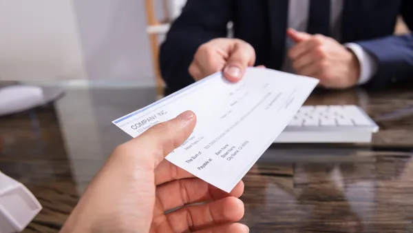 Image of business person's hand extending a paycheck to another business person.