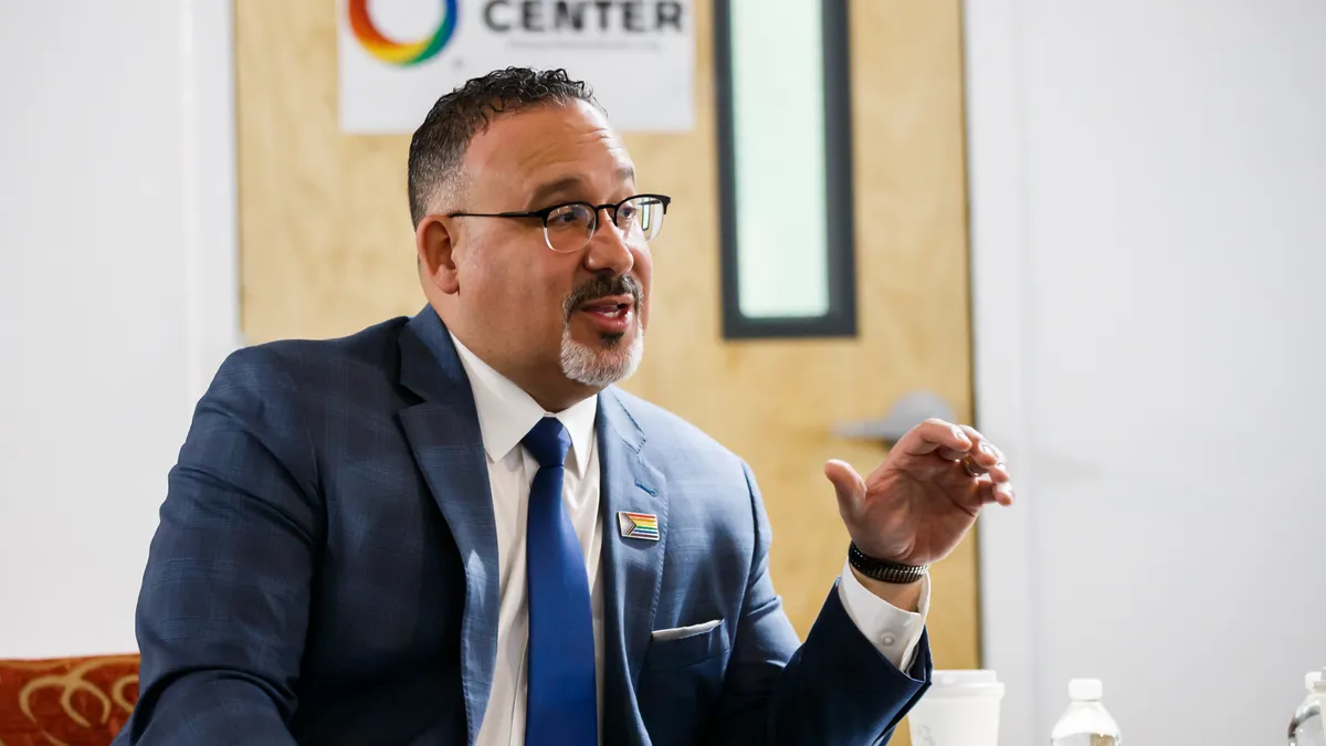 U.S. Secretary of Education Miguel Cardona sits in front of a group with his hand raised at the Orlando LGBTQ+ Center