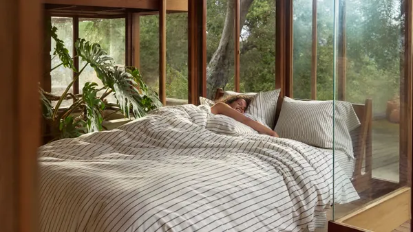A person lays in a bed with striped sheets from the Target x Parachute collection.