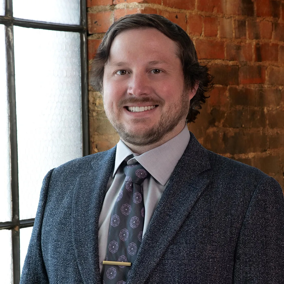 A man with brown hair in a dark blue suit.