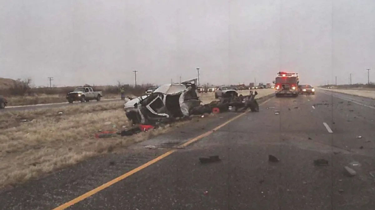 A crash photo showing the wreckage of a 2014 crash between a pickup truck and a tractor-trailer. A fire truck is shown in the background and the wreckage was resting primarily in a grassy median. Debris was shown across the road.