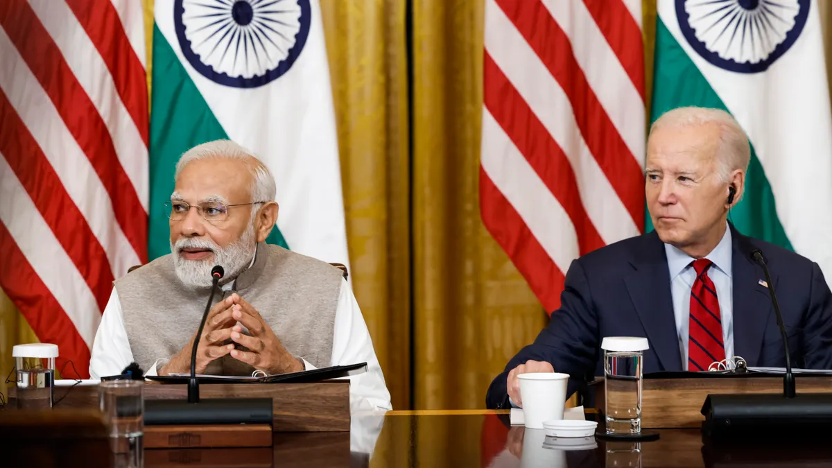 The prime minister of India sits next to the president of the United States with the countries' respective flags in the background.