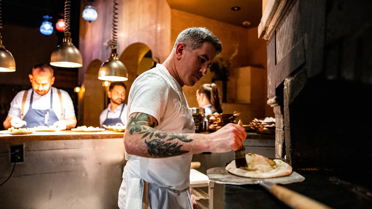 Michael Solomonov spreads olive oil on a piece of flatbread inside a restaurant kitchen