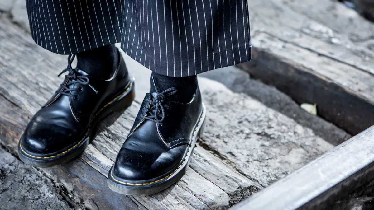 A closeup of a person's Dr. Martens oxfords. They are wearing black socks and wide legged striped pants.