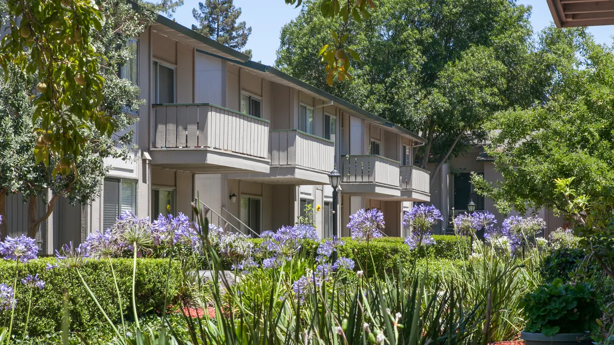 Brown, two story apartments surrounded by trees and flowers