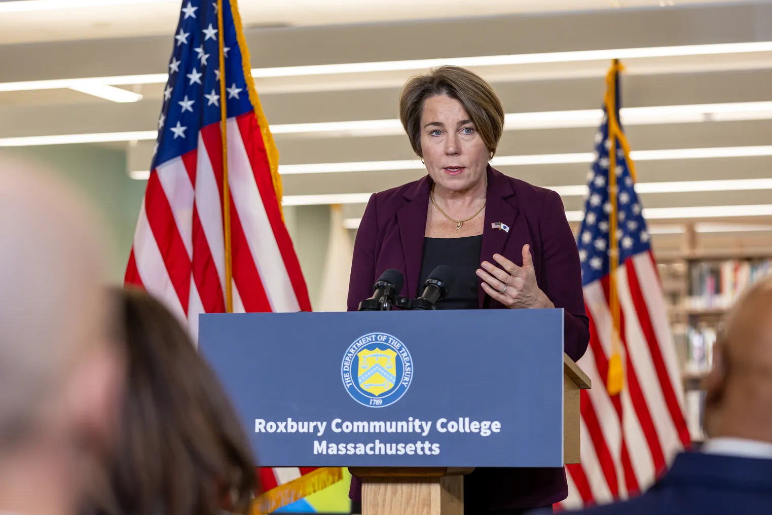 A woman with a short hair cut speaks at a podium that say "Roxbury Community College Massachusetts."