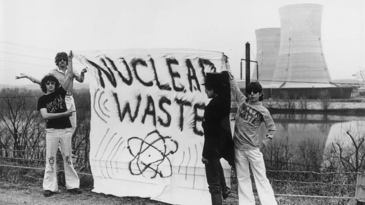 Four people hold a banner reading 'nuclear waste' outside a power plant