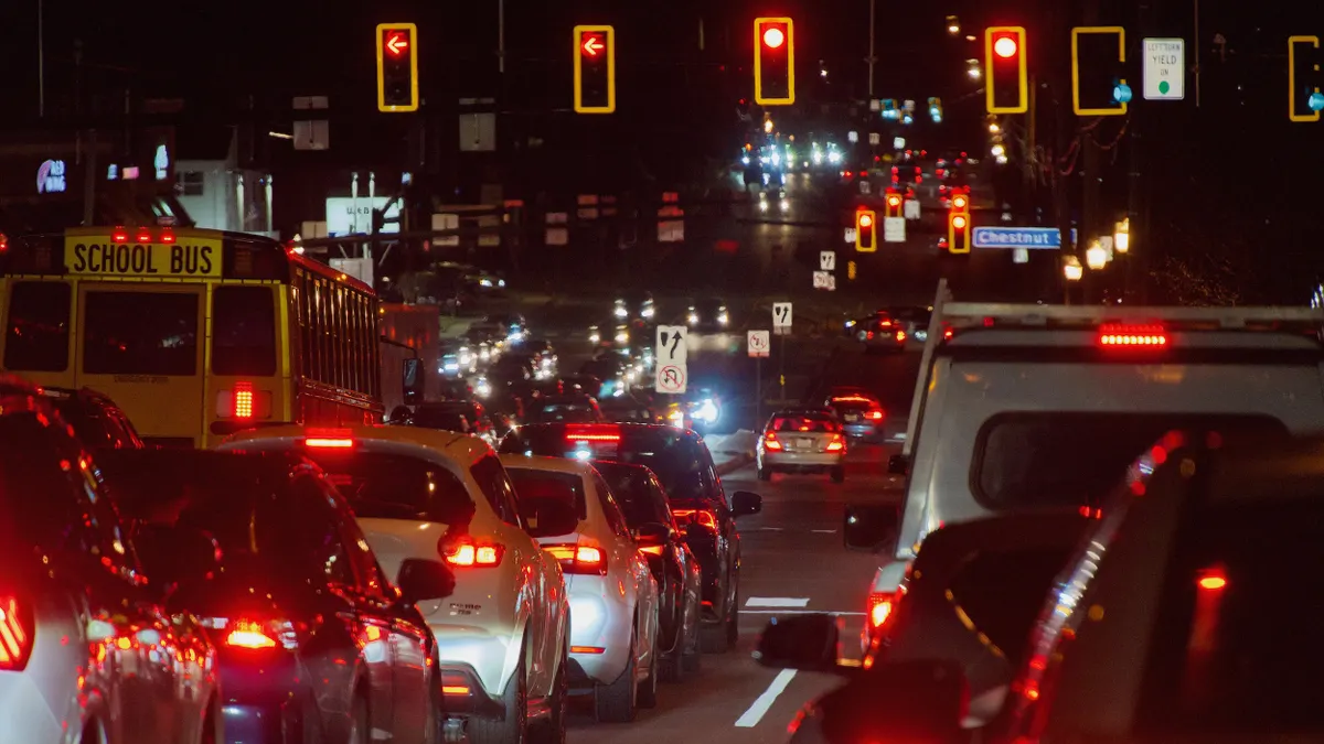Night scense of a multilane road filled with cars and a school bus stopped at a red light.