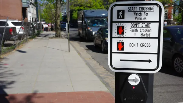A sign at a crosswalk with a push button.
