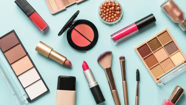 Skin tone palette, lipsticks, makeup brushes, eyeshadow palettes and nail polish on a sky blue background.