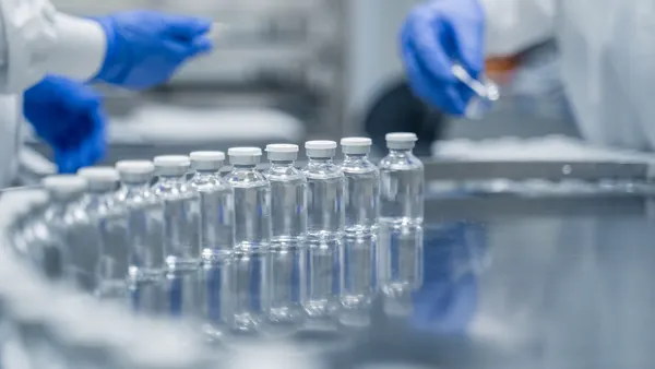 Gloved workers supervise rows of glass bottles on a pharmaceutical production line.