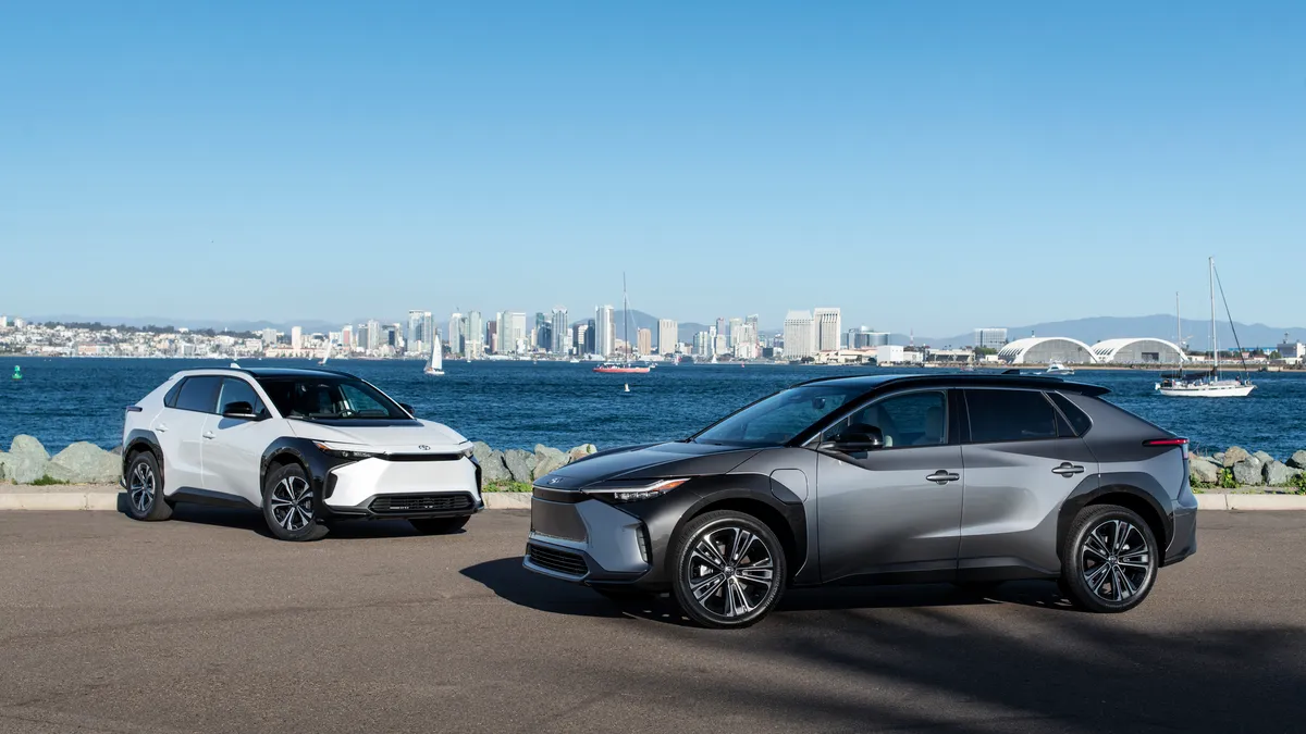 A pair of Toyota bZ4X SUVs parked at a waterfront with a city skyline in the background.