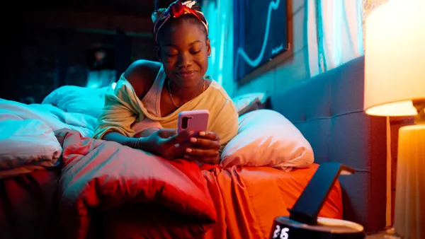 A Black woman looks at her phone while sitting on a bed in an image from Gilead’s “Up to Date” HIV prevention campaign.