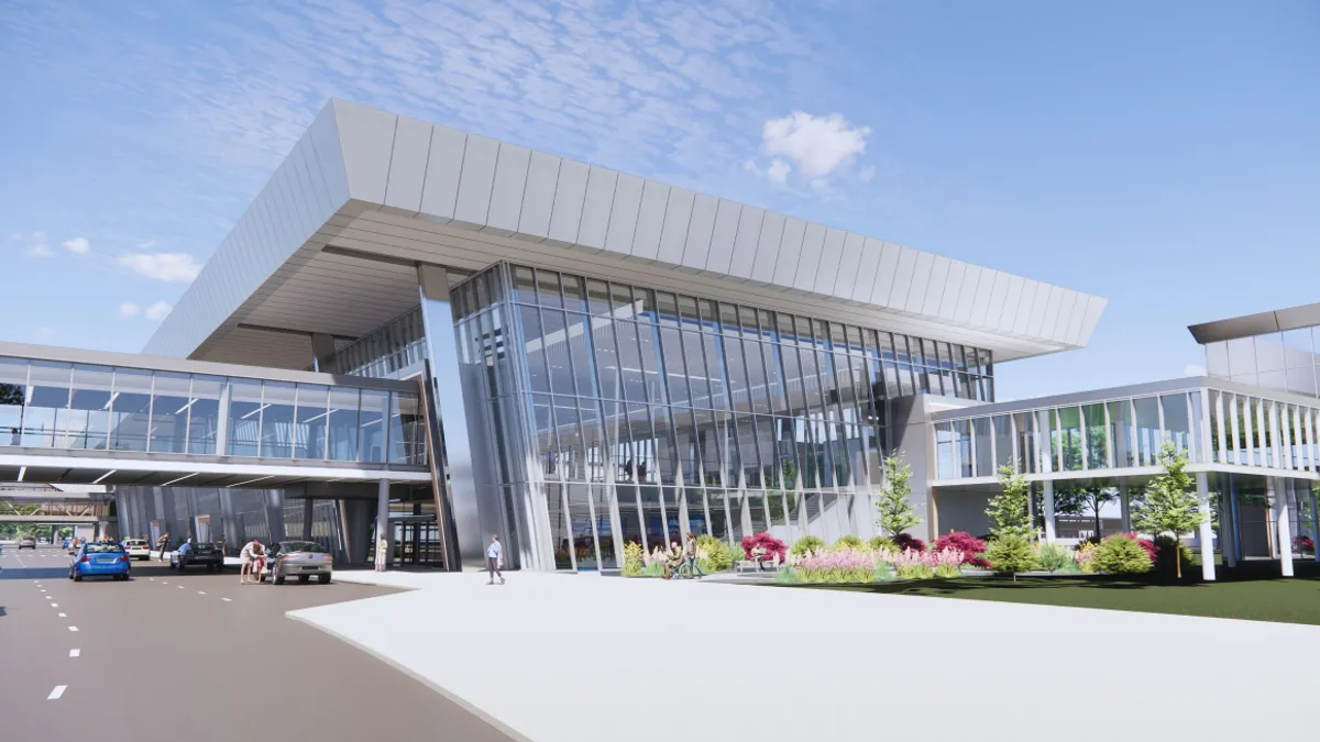 Outside view of a glassy building with a walkway on the left over a roadway.