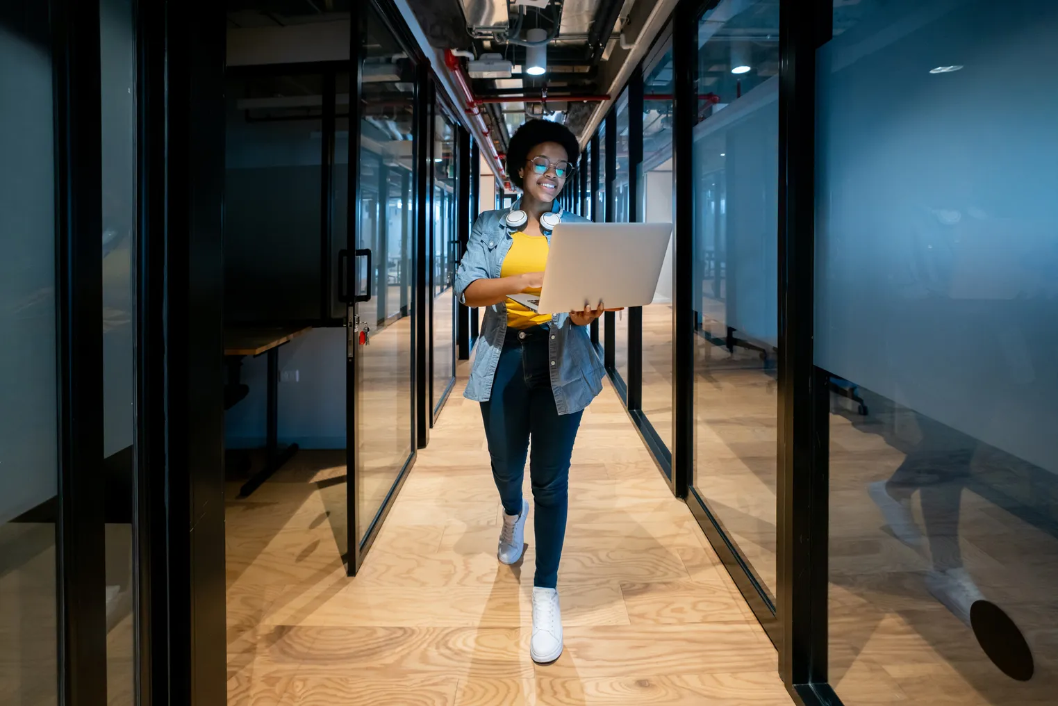 A worker walks in a tech firm office with a laptop.