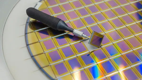 Silicon wafer with microchips, fixed in a holder with a steel frame on a gray background after the process of dicing.