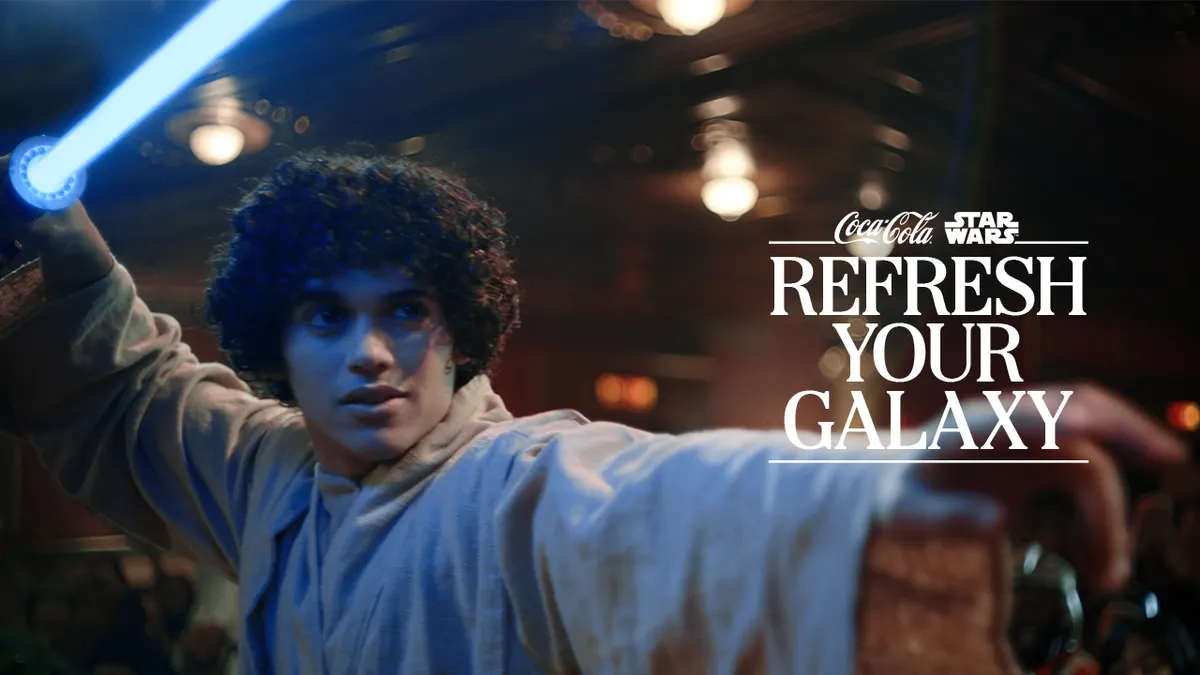A Star Wars fan dressed as a jedi holds up a blue lightsaber toy