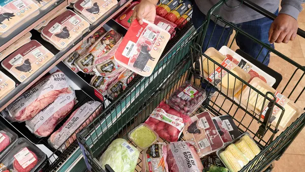 A person holds a package of meat in a grocery aisle with other types of packaged meats.