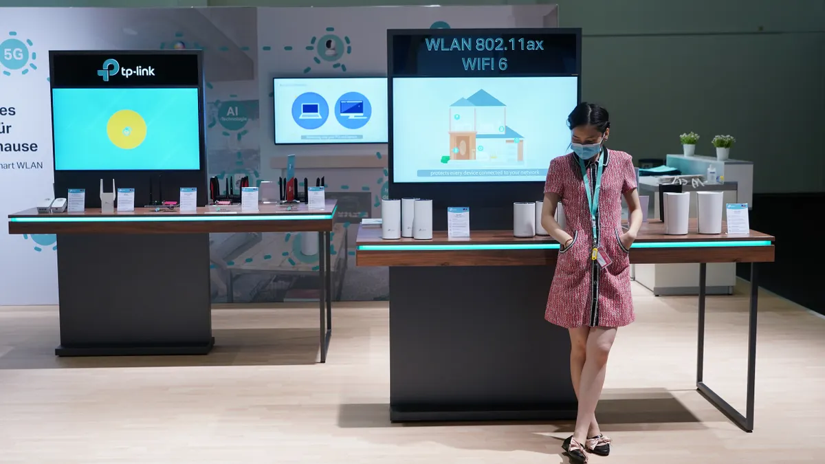 A woman wearing a surgical mask stands in front of a booth for the Chinese networking company TP-Link at a German consumer electronics trade show.