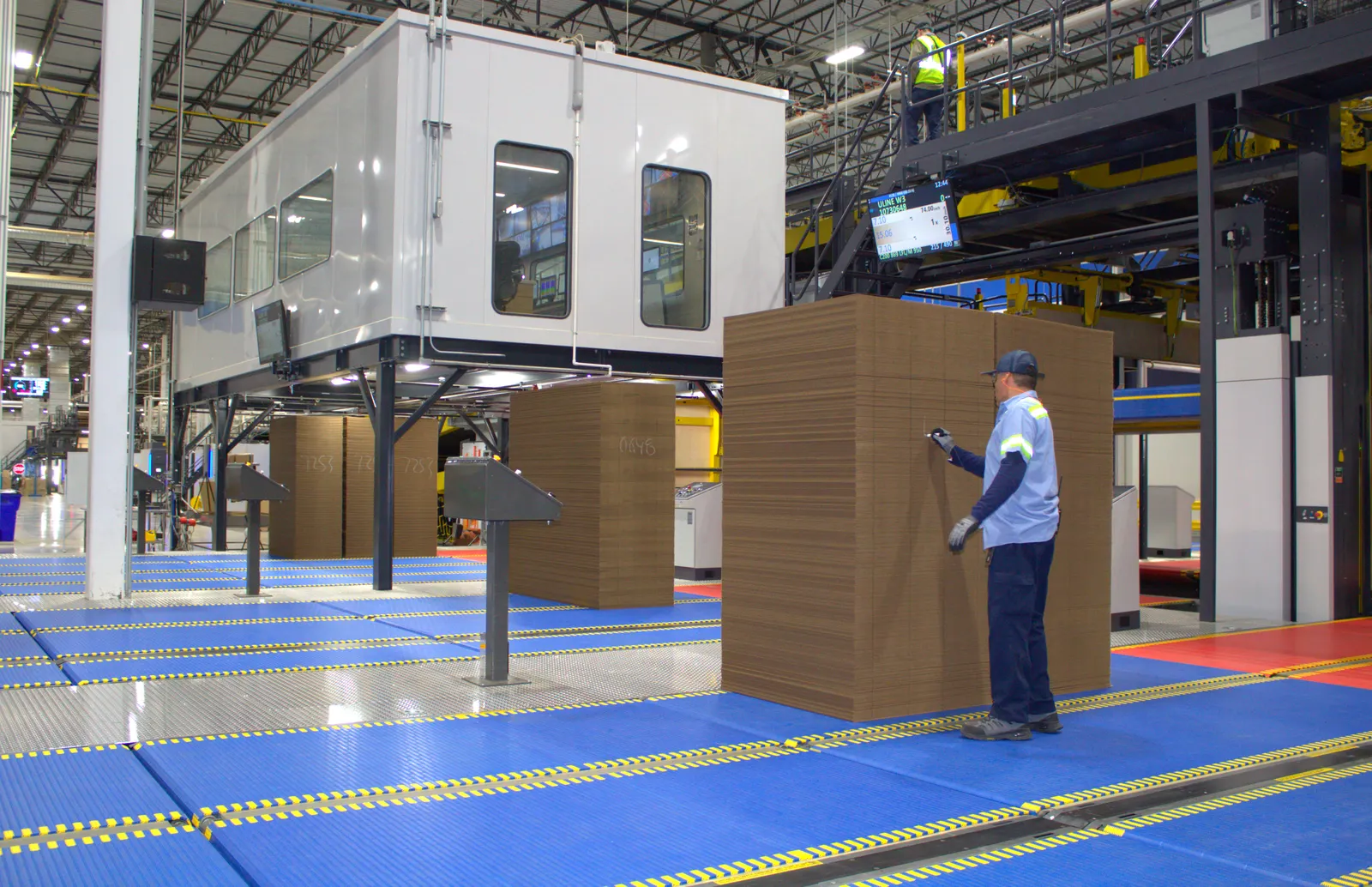 A person marks a stack of flat corrugated boxes on a conveyor in an industrial facility.