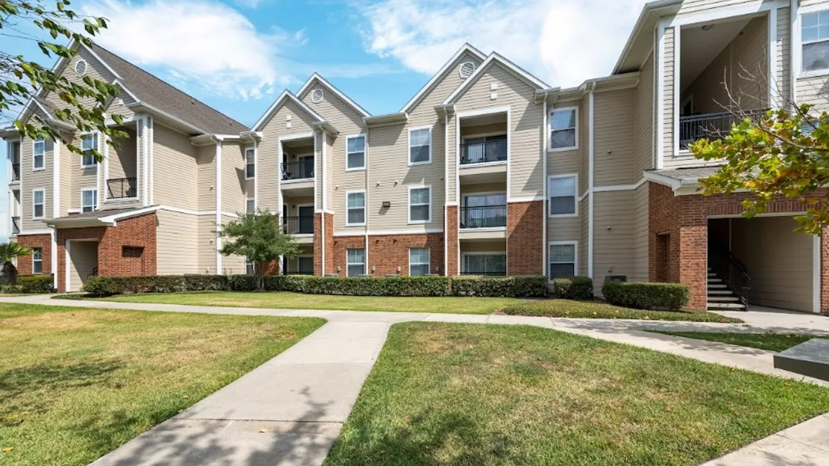 Three-story brick and tan apartment building with grass in the foreground