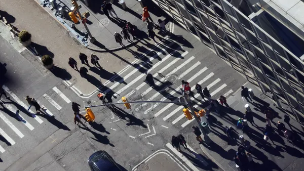 Overhead view of dozens of people crossing streets in different directions.