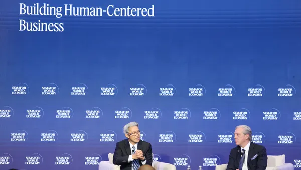 Two men speak in front of a blue panel reading "Building Human-Centered Business"