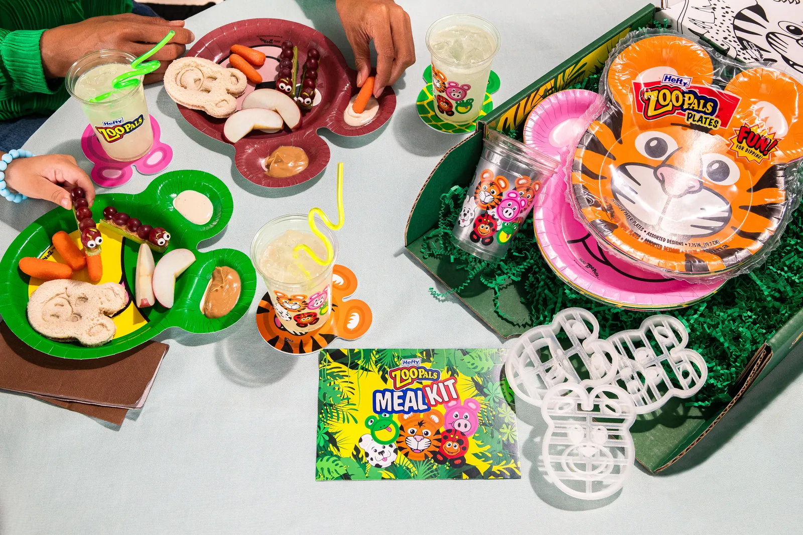 Display of Zoo Pals meal kit with animal-themed plates, cuts, coasters and sandwich cutters laid out on a colorful green table