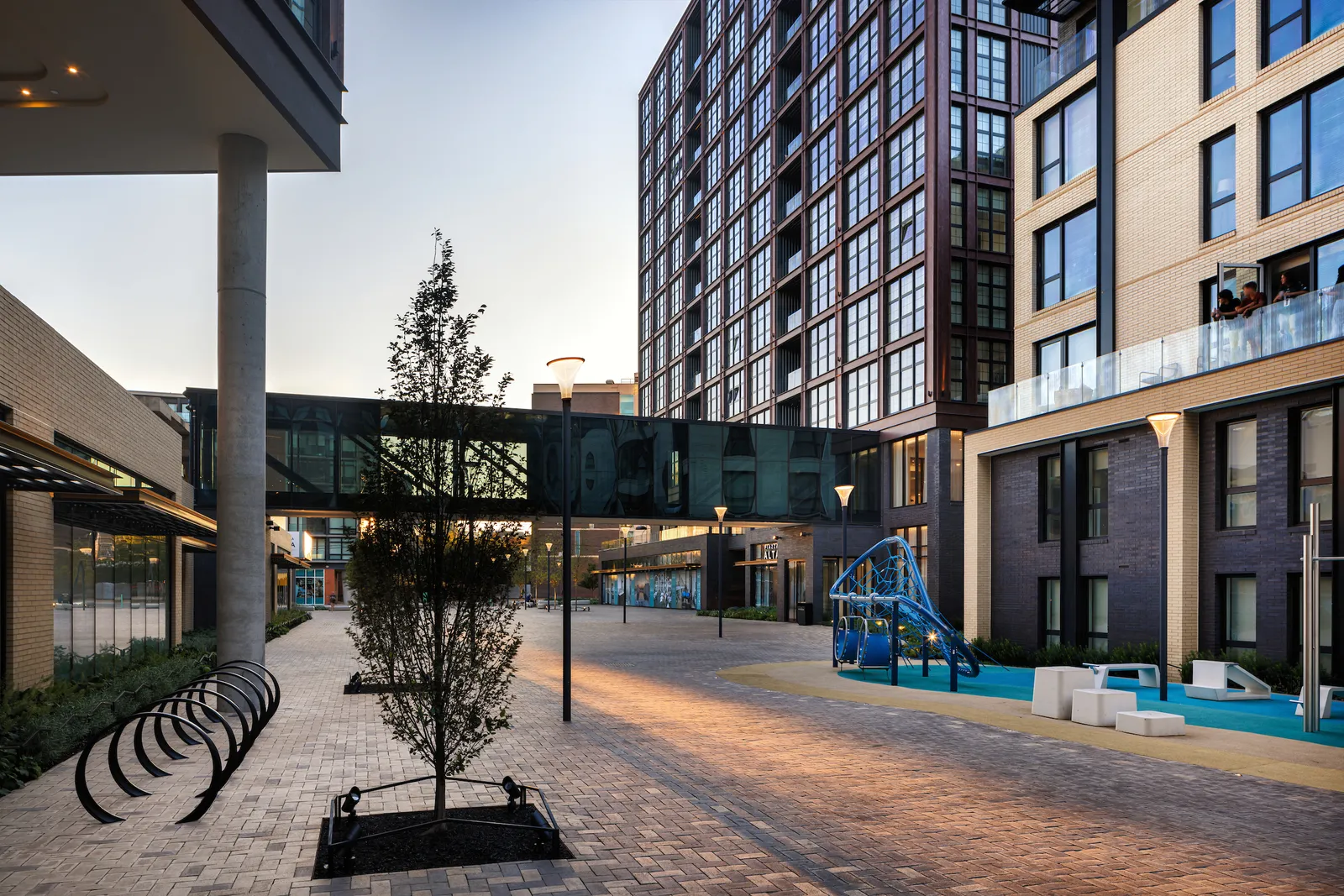 A walkway between two sets of buildings, with bike racks and a tree.