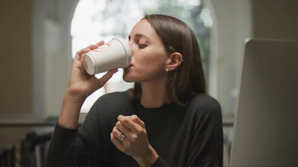 A person drinks from a fiber cup with a lid.