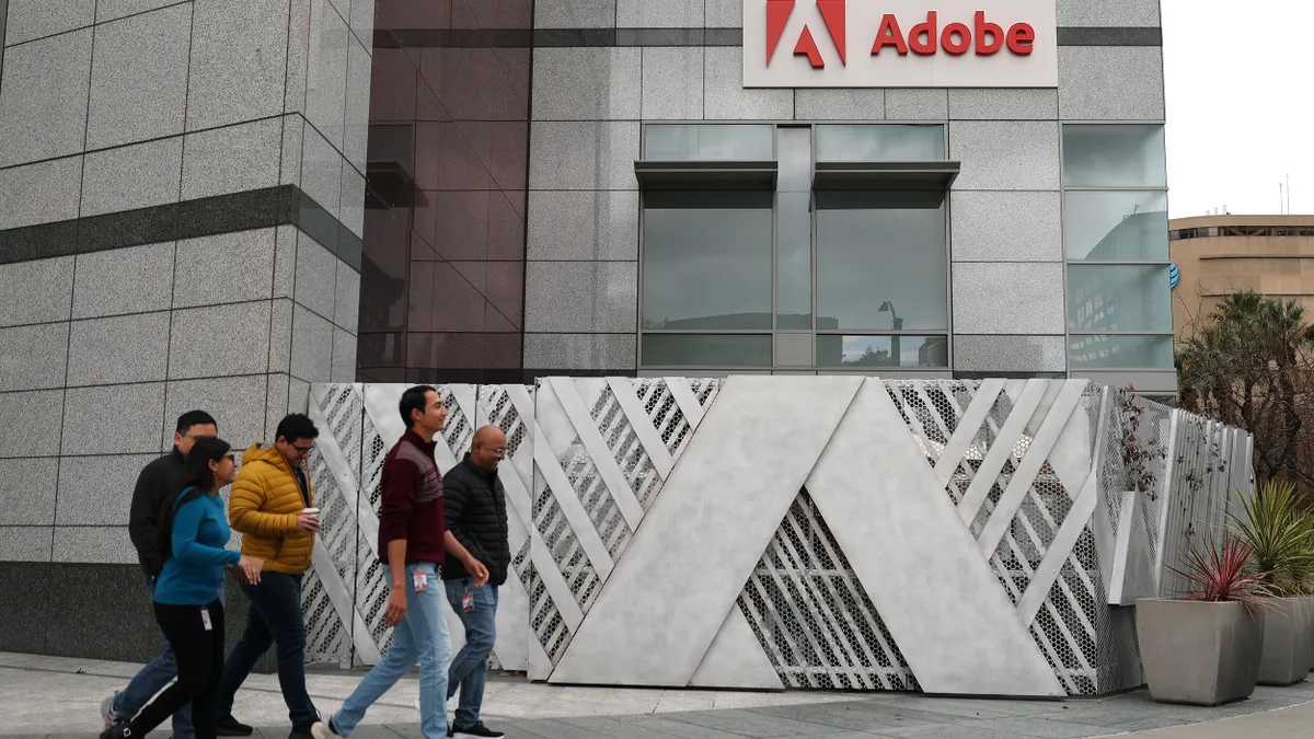 Pedestrians walk by a sign at Adobe headquarters on December 12, 2024 in San Jose, California.