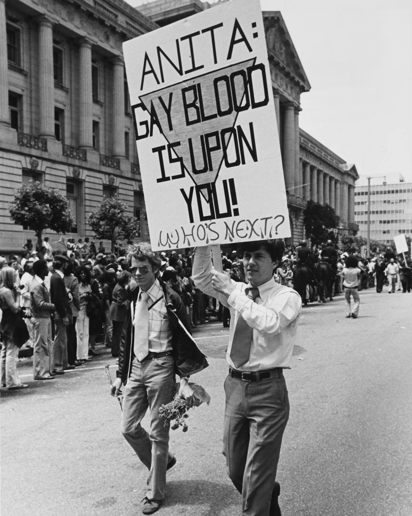 Two protestors hold a sign in the street that reads, "Anita: Gay blood is upon you! who's next."