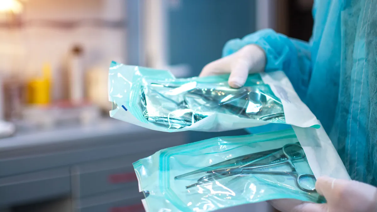 Close up of dentist hands in white sterile gloves holding dental tools for surgical use packed in a protective foil at dental office