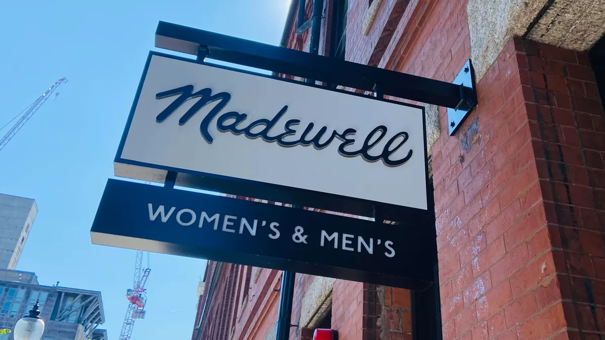 A Madewell sign sticks out from a brick building against a blue sky.