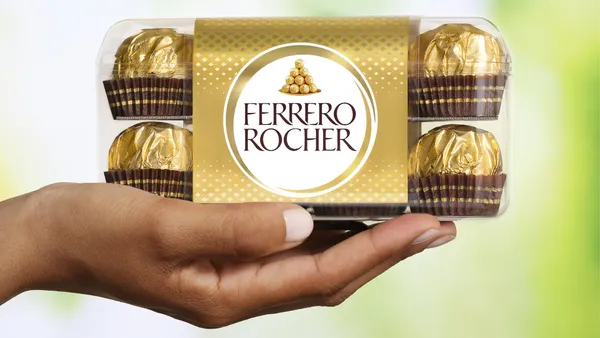 A person's hand holding a box of individually wrapped Ferrero Rocher chocolates.