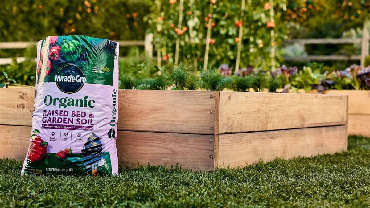 A bag of Scotts Miracle-Gro organic fertilizer sits on a lawn, in front of a garden bed.