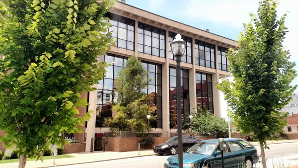 A courthouse with large windows can be seen across the street between two trees in the foreground.