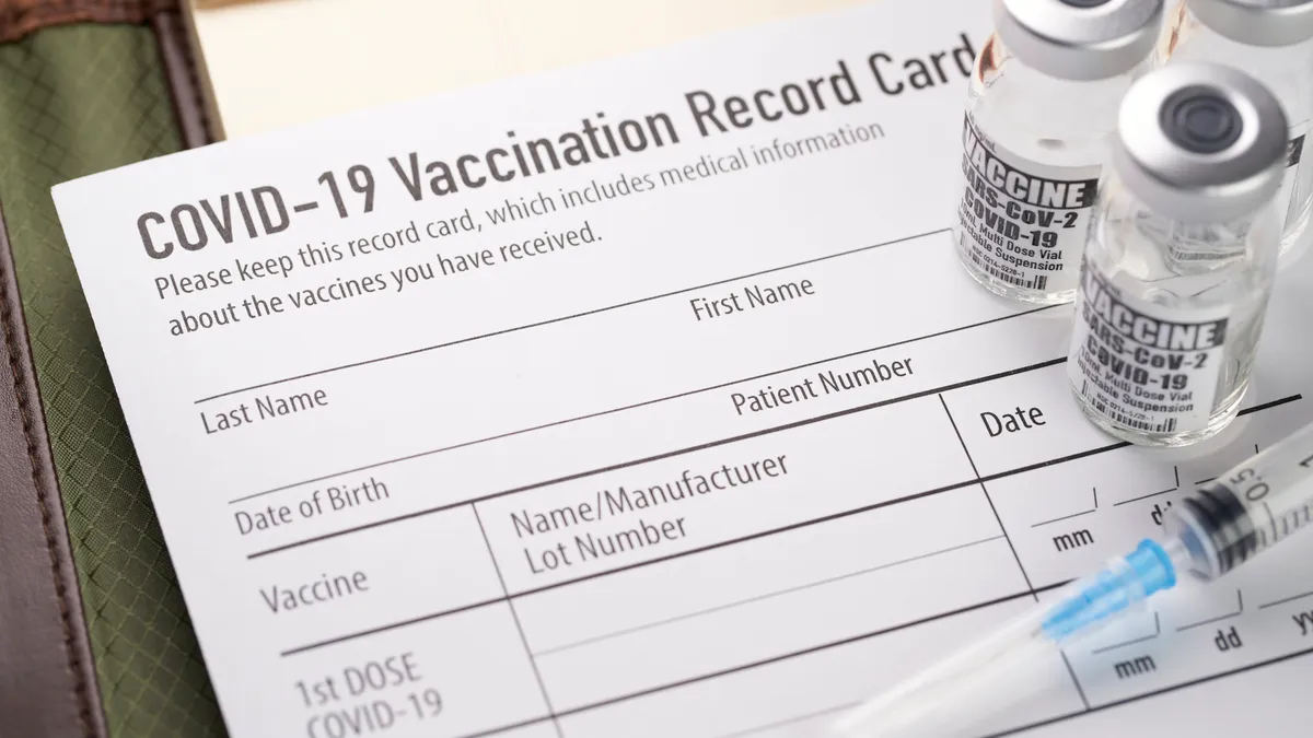 Covid-19 vaccination record card with vials and syringe. - stock photo