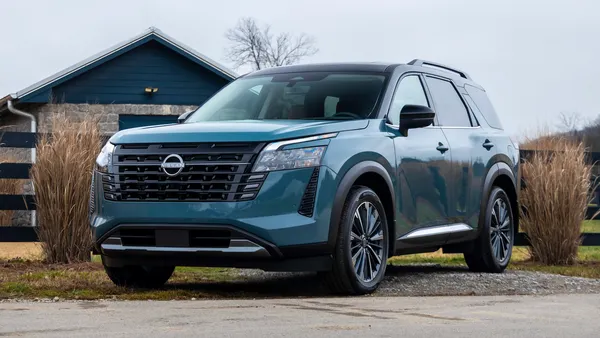 A 2026 Nissan Pathfinder SUV parked outdoors with a fence and building in the background.