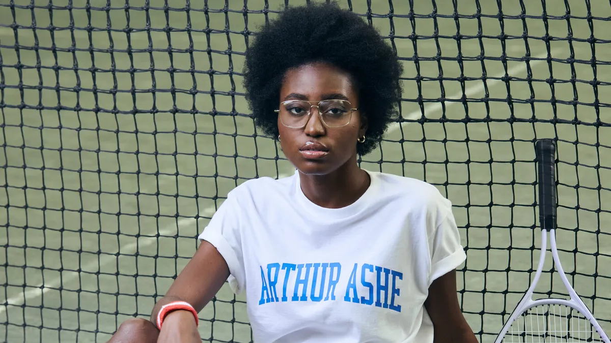 A model sits on a tennis court in front of the net.