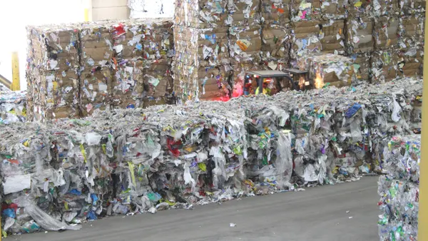 Bales of plastic film packaging are piled next to bales of other plastics and cardboard.