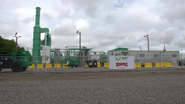 A new industrial facility and a trailer sit behind a chain-link fence. A sign on the fence has the Archaea Energy and Rumpke logos.