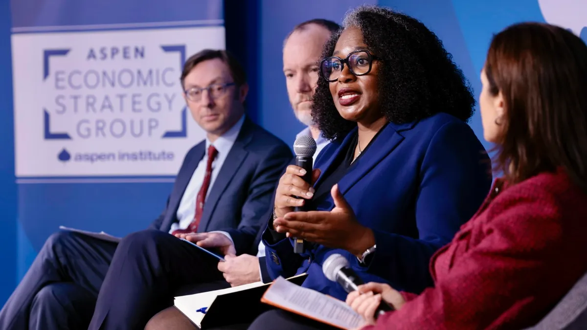 Four people are sitting in a row. One person has a microphone and the others are looking at the person.