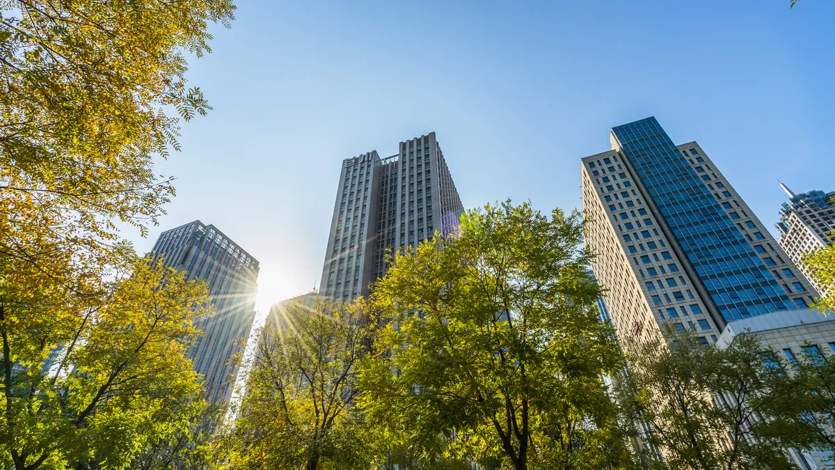 A city skyline during the day with several office buildings behind trees.