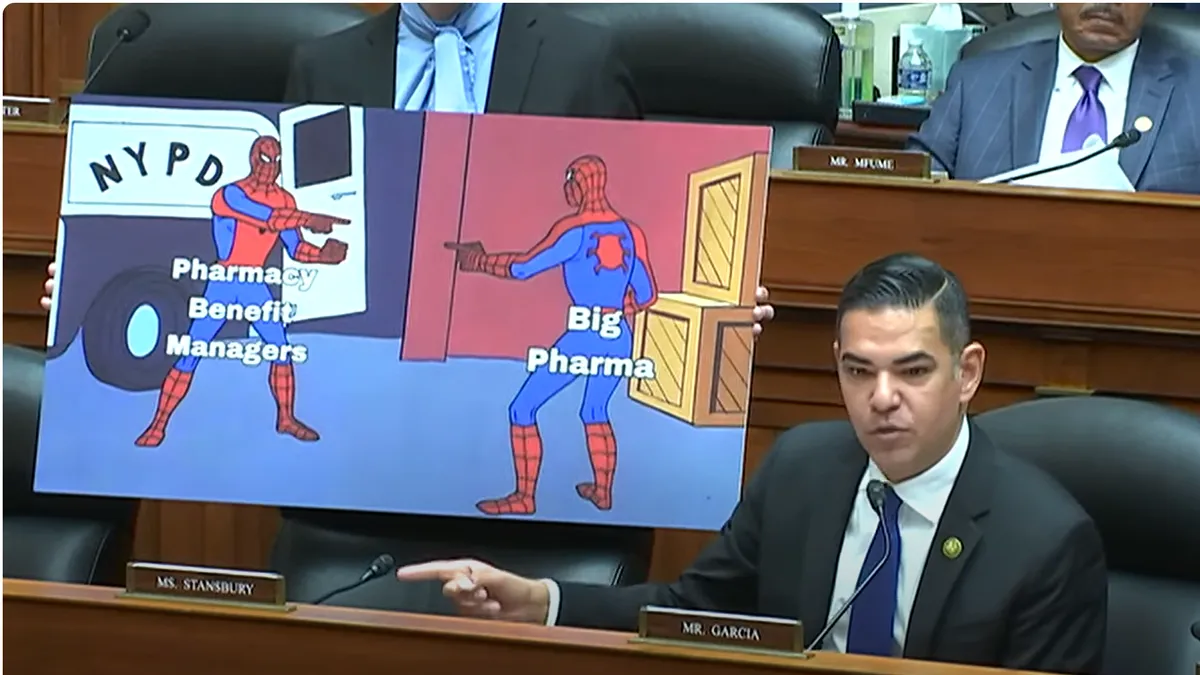 Congressman Garcia gestures to a cardboard meme of two identical Spiderman characters pointing at one another.