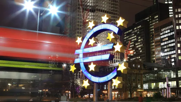 A tram passes the giant Euro symbol with high rise office buildings the city of Frankfurt am, Germany in the background