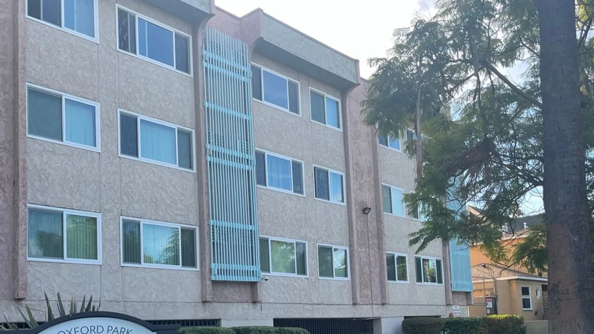 Three-level tan apartment with a tree on the right.