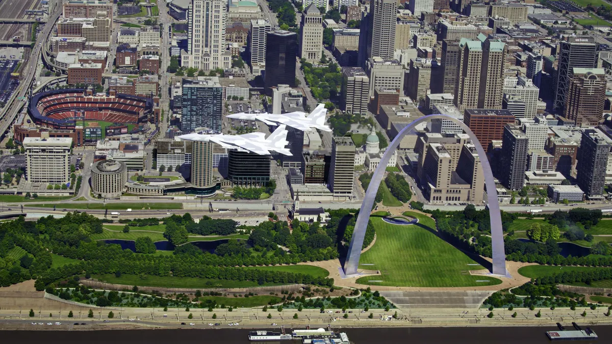 Two bright gray and white fighter jets flying over the Gateway Arch in St. Louis.